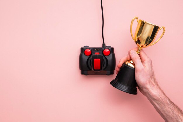 Mano de jugador ganadora usando un joystick de juegos retro con un trofeo ganador de oro