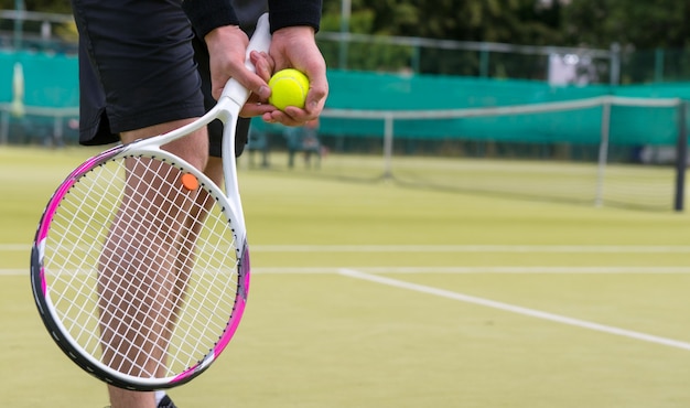 La mano del jugador masculino con pelota de tenis preparándose para servir al aire libre en una cancha de tenis