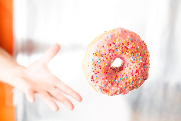 La mano lanza y atrapa una rosquilla rosa con cobertura de pastelería glaseada