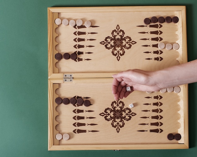 Una mano lanza un hueso blanco sobre un tablero de backgammon.