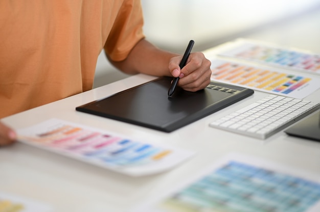 Foto mano con lápiz escribiendo en pizarra digital con carta de colores en el escritorio del diseñador