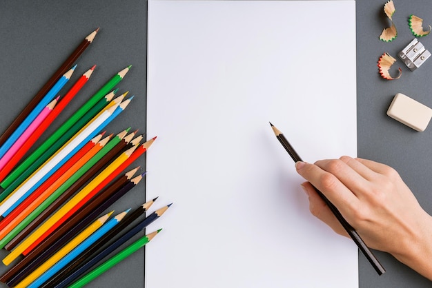 mano con un lápiz sobre un fondo gris y un juego de lápices de colores