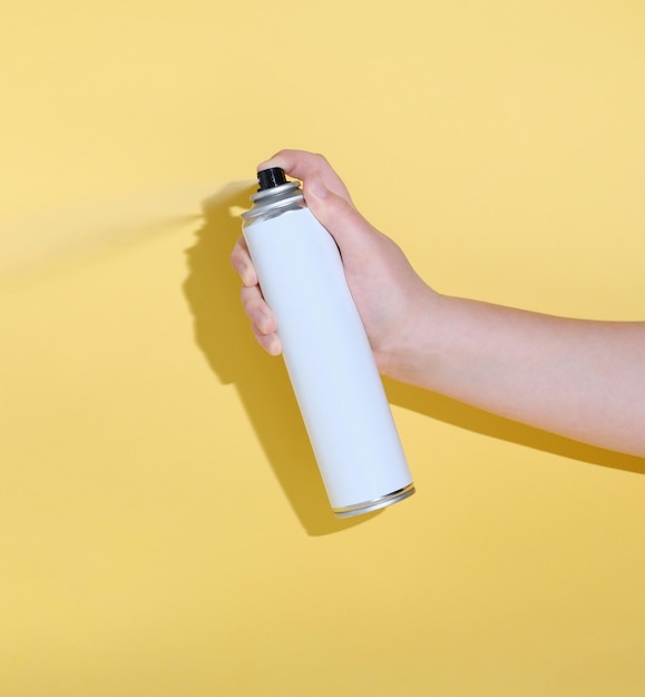 Con la mano una lata y rociando un producto sobre un fondo amarillo para la limpieza del diseño