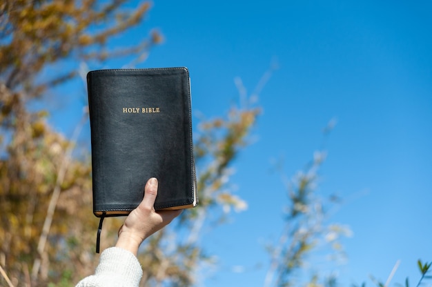 Foto mano levantada sosteniendo la santa biblia