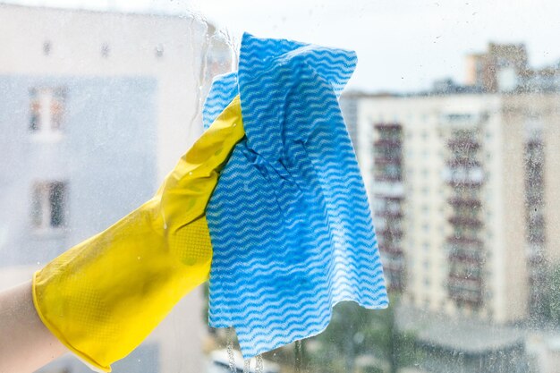 La mano limpia el vidrio de la ventana de la casa en la casa urbana