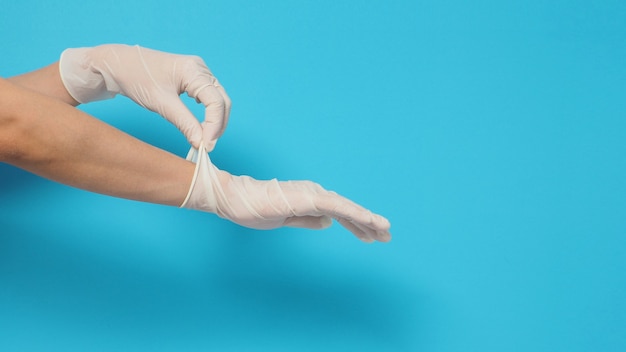 La mano lleva guantes quirúrgicos blancos o guantes de látex sobre un fondo azul o turquesa.