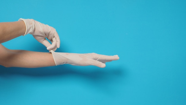 La mano lleva guantes quirúrgicos blancos o guantes de látex sobre un fondo azul o turquesa.