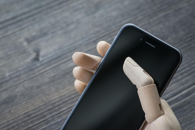 Mano de madera artificial con teléfono moderno en tablero de madera