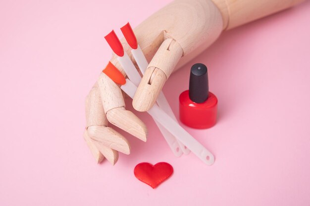 Mano de madera cerca de la paleta roja para uñas de manicura y diseño de corazón de esmalte de gel