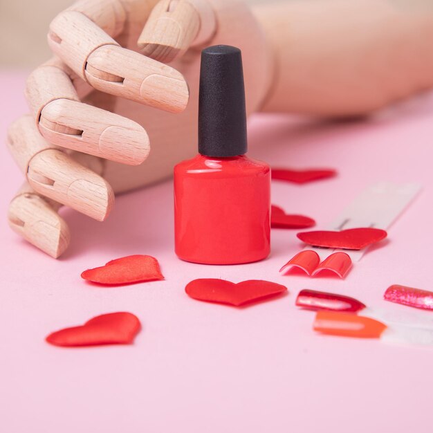 Mano de madera cerca de la paleta roja para uñas de manicura y diseño de corazón de esmalte de gel