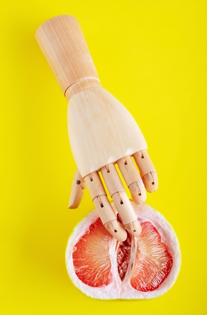 Mano de madera con la mitad de pomelo sobre fondo amarillo