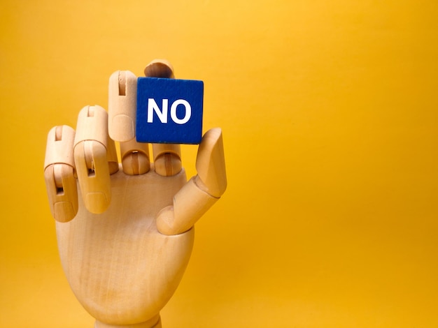 Mano de madera sosteniendo cubo azul con la palabra NO sobre fondo amarillo Concepto de negocio