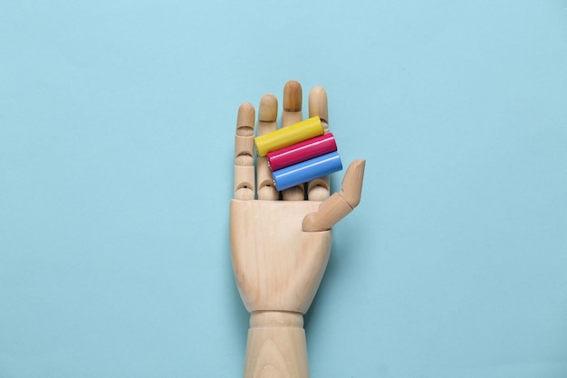 La mano de madera sostiene pilas aa de colores sobre un fondo azul.