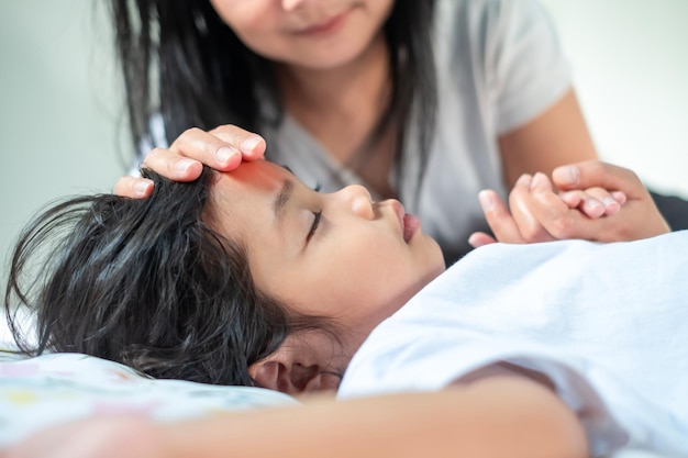 La mano de la madre descansa sobre la frente de su hijo y sostiene la mano mientras ella está enferma cuidando enfermarse Concepto médico y de salud