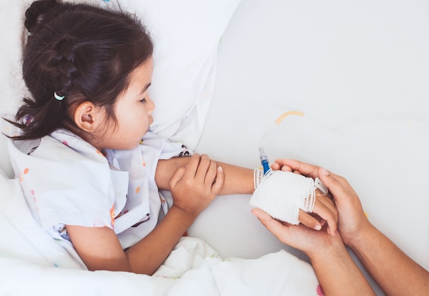 Mano de la madre sosteniendo la mano hija enferma que tiene solución IV vendada