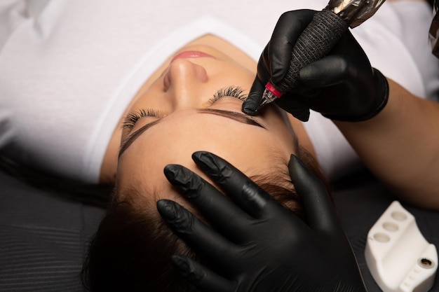 Foto mano del maestro de cosmetología haciendo maquillaje permanente