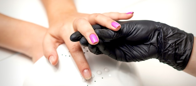 La mano del maestro de manicura sostiene un dedo femenino con esmalte de uñas púrpura mientras pinta las uñas en un salón de uñas