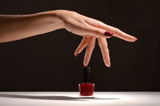 Mano con manicura roja y botella de esmalte de uñas