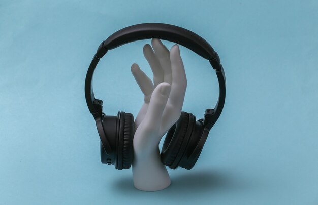 Foto mano de maniquí blanco con auriculares se encuentra sobre fondo azul.