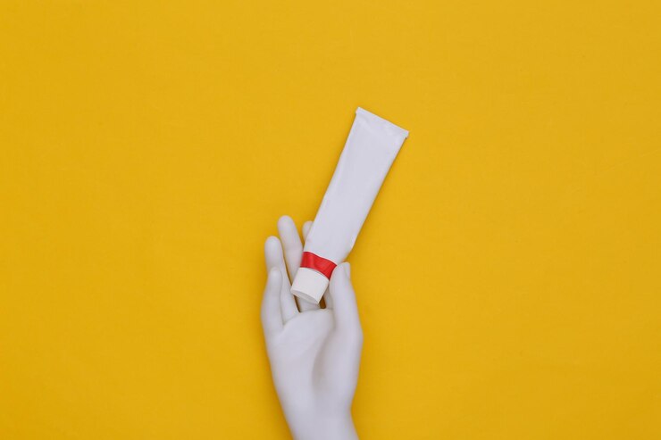 Foto la mano del maniquí sostiene un tubo de crema o pasta de dientes contra un fondo amarillo. vista superior