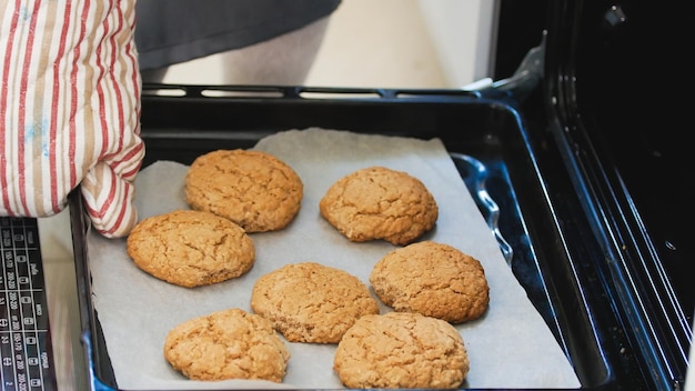 La mano en la manopla saca del horno las galletas caseras de cerca