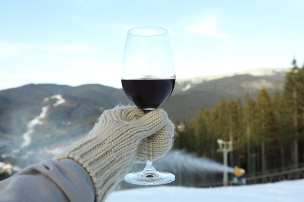 Mano en manopla sostiene una copa de vino contra las montañas