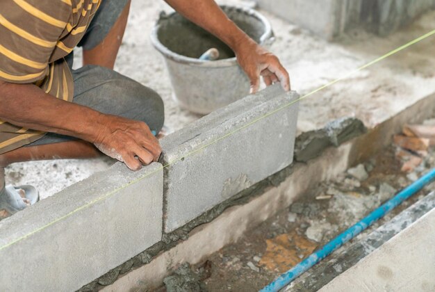 La mano de la mansión instala ladrillo de hormigón para la pared del edificio en el sitio de construcción