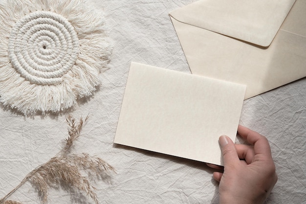 La mano de la maqueta de Minumal sostiene la tarjeta blanca Sobre macramé y hierba de la pampa