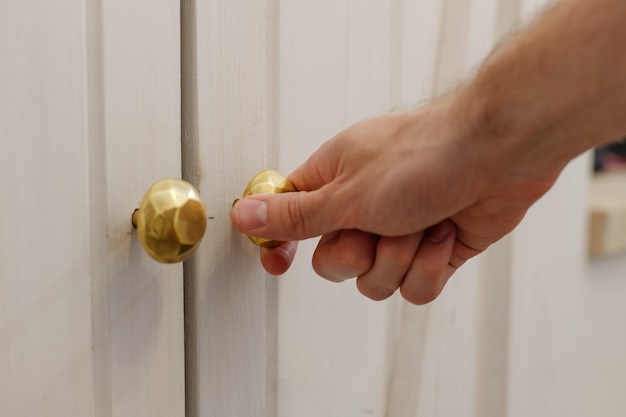 Mano masculina abre la puerta del armario de pared blanca.