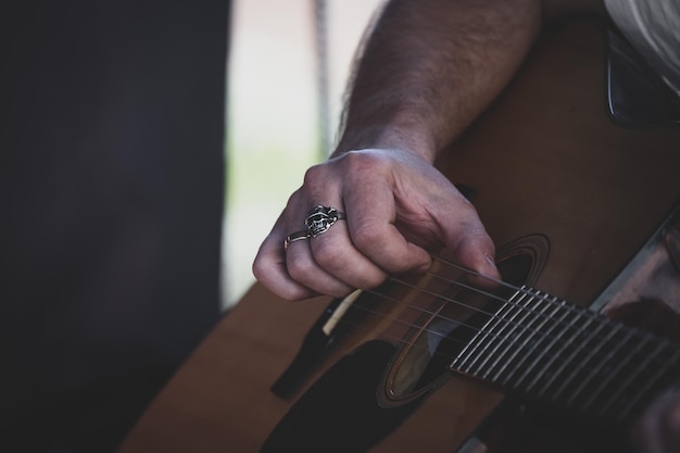 Mano masculina con anillo de calavera tocando guitarra closeup Tocar la guitarra La mano de un hombre toca las cuerdas