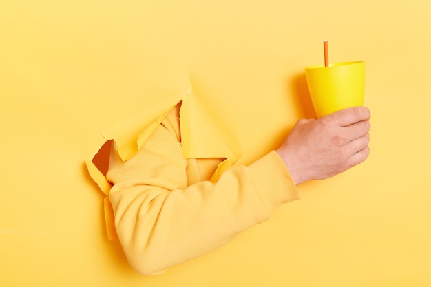 Mano masculina desconocida sosteniendo una taza de cóctel fresco en una taza con paja aislada sobre fondo amarillo brillante Banner