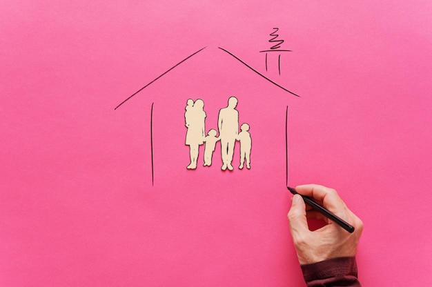 Mano masculina dibujando una forma de casa alrededor de una silueta familiar de corte de papel de cinco en una imagen conceptual de seguridad y refugio