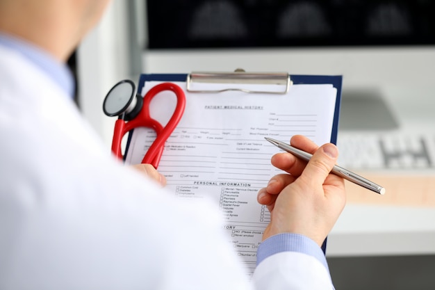 Mano masculina del doctor de la medicina que lleva a cabo la escritura de plata de la pluma algo en el primer del tablero. Sala redonda, control de visita del paciente, cálculo médico y concepto de estadísticas. Médico listo para examinar al paciente.