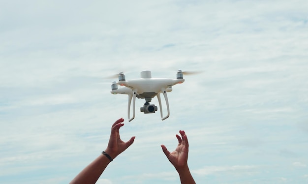 Mano masculina con drone blanco flotando en un cielo azul brillante