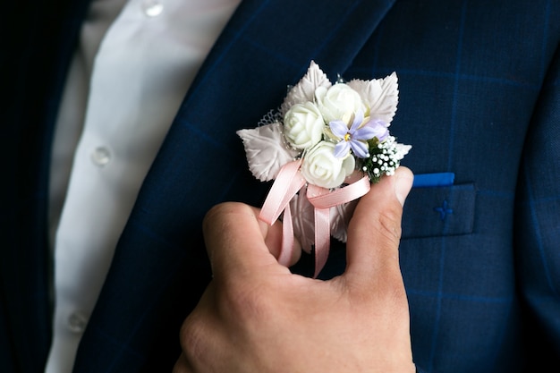 Mano masculina endereza el boutonniere en el traje del novio.