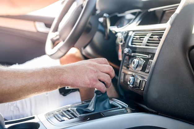 Mano masculina en el engranaje de transmisión dentro del coche. Cerrar vista de mano masculina con interior de coche