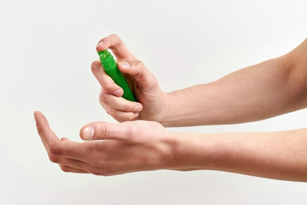 La mano masculina está rociando desinfectante para manos. Prevención del virus. Fondo claro, primer plano.