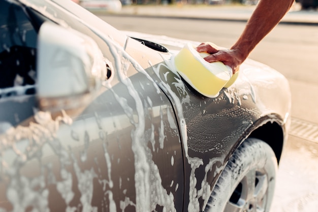 Mano masculina frotando el coche con espuma, carwash