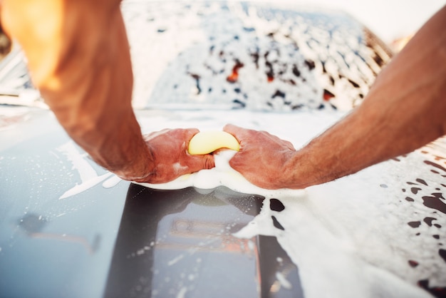 Mano masculina frotando el coche con espuma, carwash