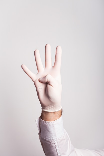 La mano masculina en un guante médico muestra cuatro dedos en una pared blanca
