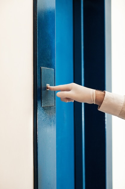 Una mano masculina en un guante médico presiona un botón en el elevador