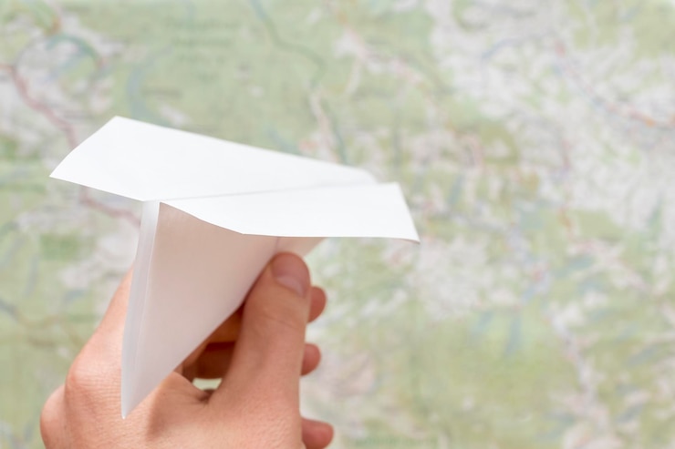 Foto mano masculina lanza un avión de papel en el fondo del mapa