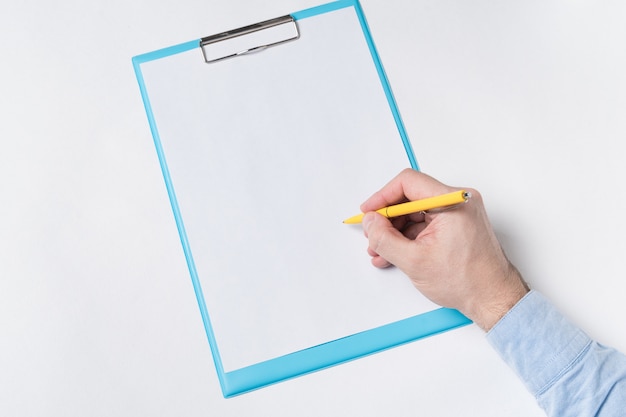 Mano masculina con lápiz en una hoja de papel en blanco. El hombre pone firma en papel.