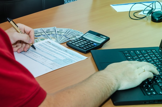 Mano masculina llena formularios de impuestos 1040 en el escritorio de la oficina