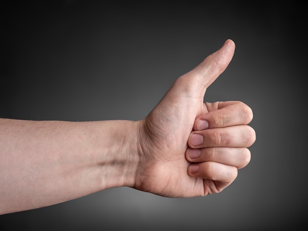 La mano masculina muestra el pulgar hacia arriba en la pared gris.