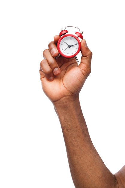 Mano masculina negra que sostiene el reloj de alarma en miniatura rojo, aislado en el fondo blanco. Sueño, concepto de gestión del tiempo