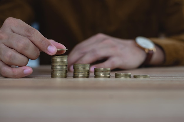 Mano masculina poniendo dinero moneda pila creciente negocio en mesa de madera Demuestra el crecimiento de los ahorros