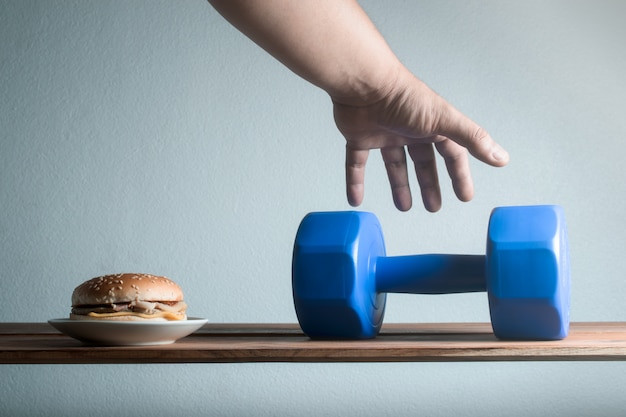 La mano masculina que alcanza para recoger los ejercicios de la idea de la pesa de gimnasia para el concepto de la dieta de la pérdida de peso.