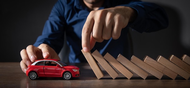 Mano masculina que evita que los bloques de madera caigan en un coche de juguete rojo