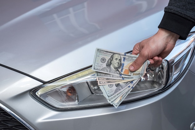 Mano masculina que muestra un dólar por comprar un coche en el autohouse. Finanzas